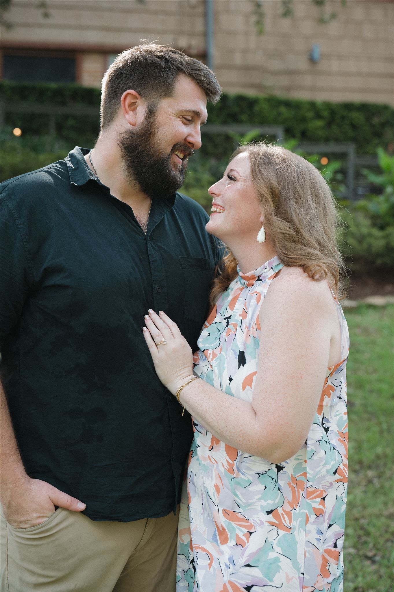 A couple shares a joyful moment together outdoors, with the woman wearing a floral dress and the man in a navy shirt.