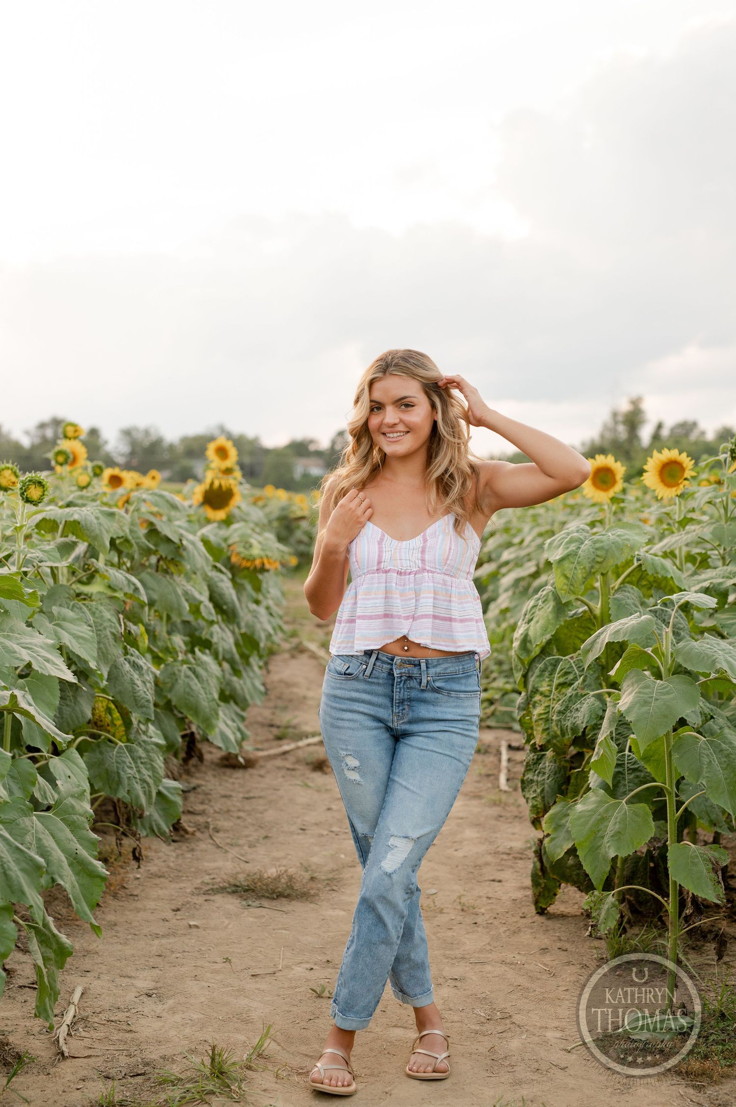 A cheerful outdoor portrait between rows of blooming sunflowers on a cloudy day.