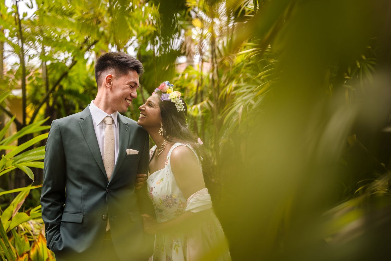 A romantic couple shares an intimate moment surrounded by lush tropical greenery.