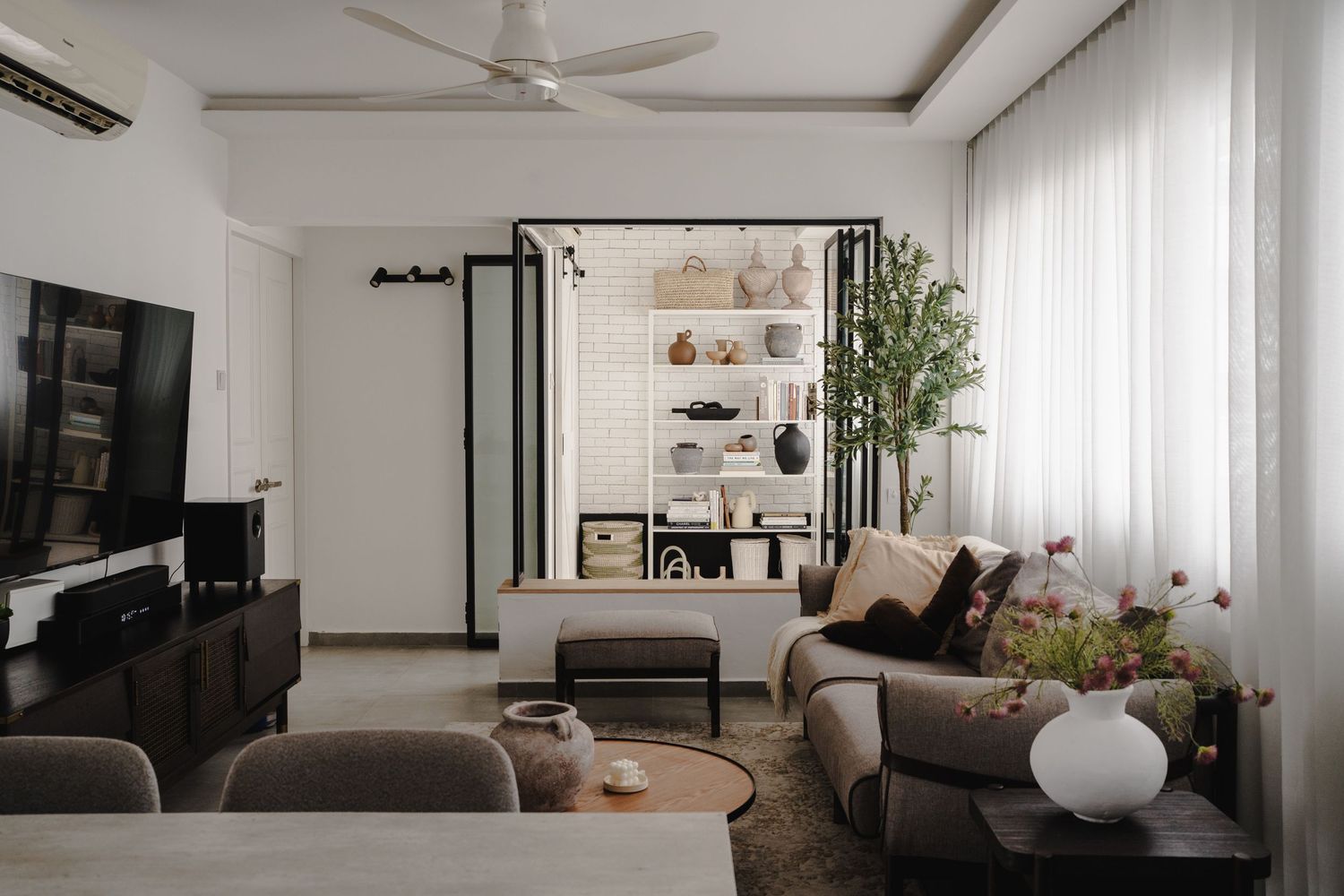 Modern living room interior with grey sofa, TV unit and decorative plants.