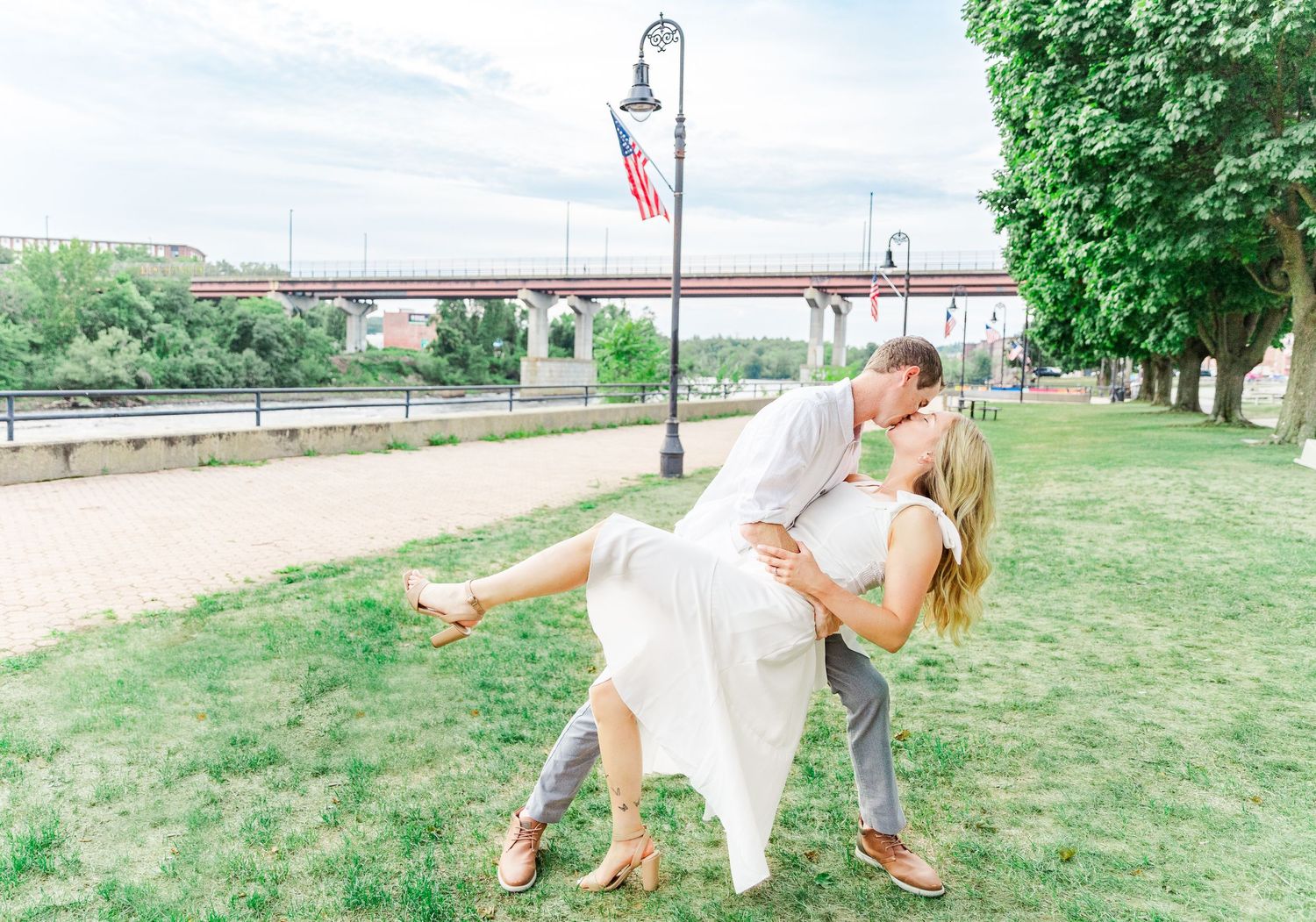 Romantic couple dancing near a lamppost in a park with American flag.