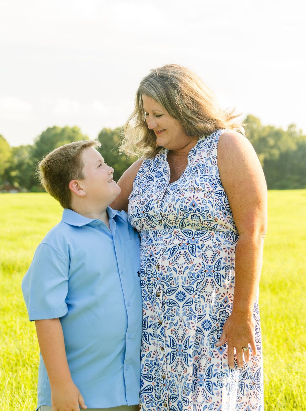 A tender portrait of a parent and child standing together in a sunlit field.