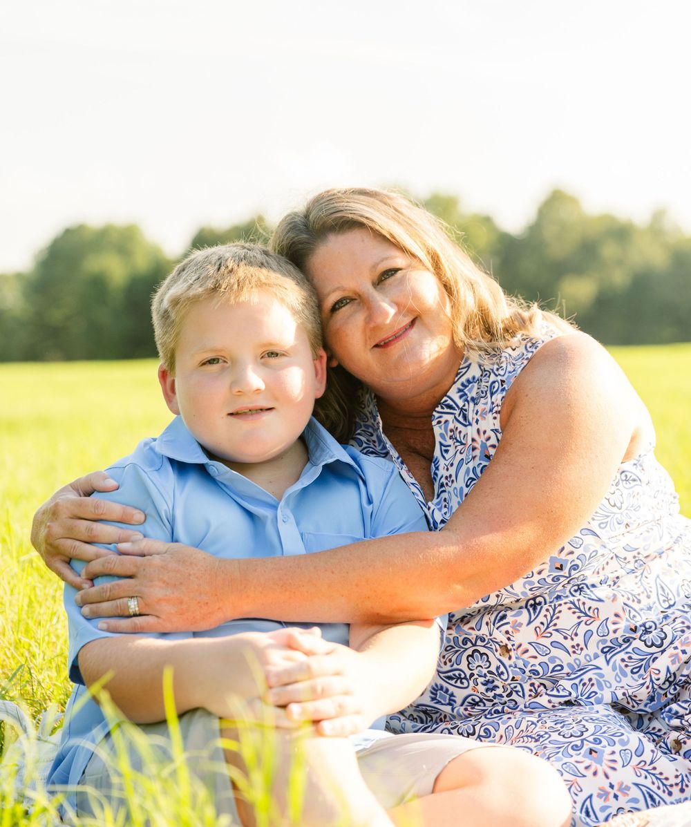 A sunny outdoor portrait capturing a tender family moment in a grassy field.
