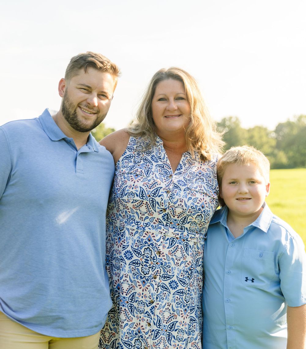 A cheerful family portrait outdoors with three people wearing coordinating blue outfits.