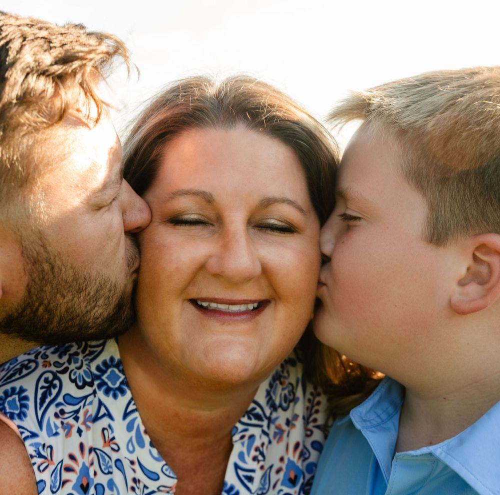 A loving family moment captured with kisses and smiles in warm sunlight.
