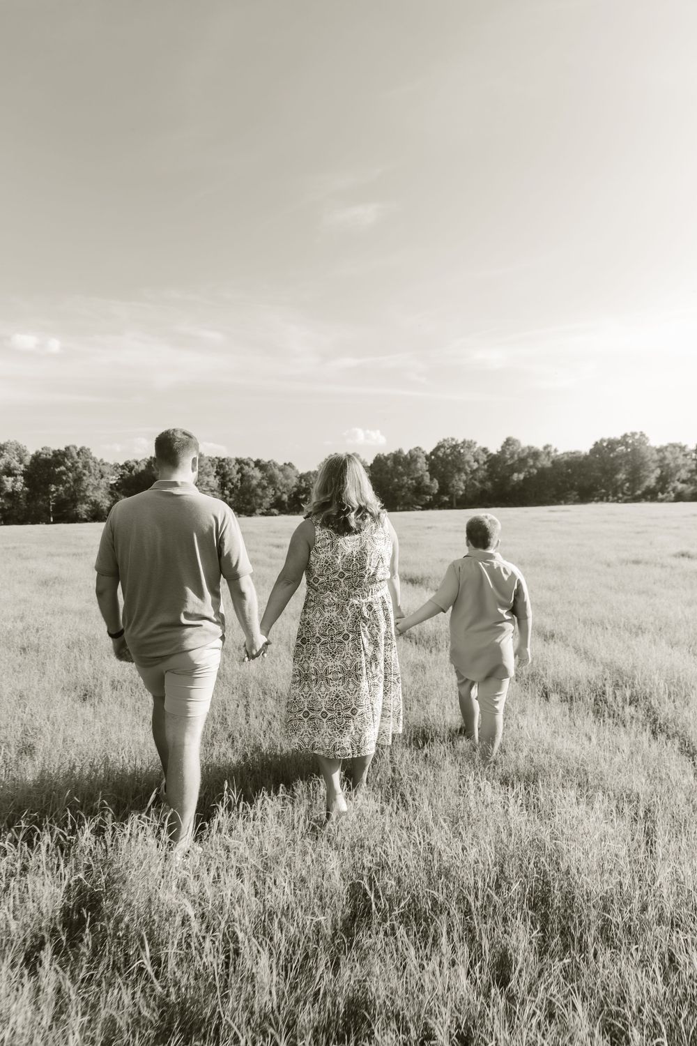A family holds hands while walking through a serene meadow in black and white.