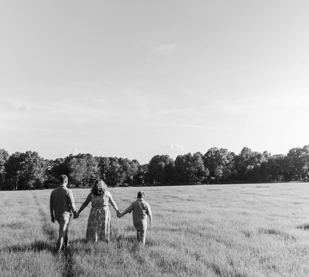 Three people holding hands while walking through a peaceful field at sunset.