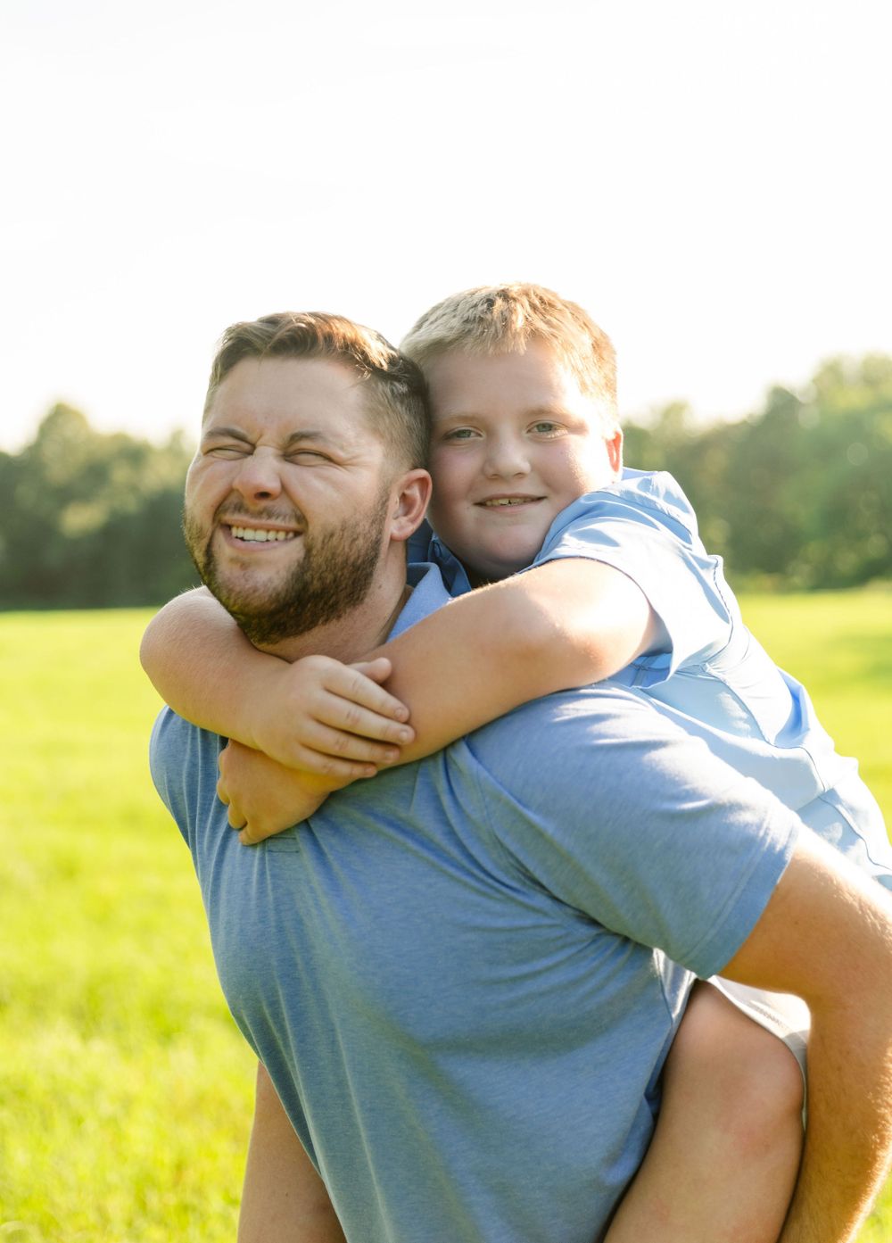 Father and son share a joyful piggyback moment while enjoying time together in a grassy field.