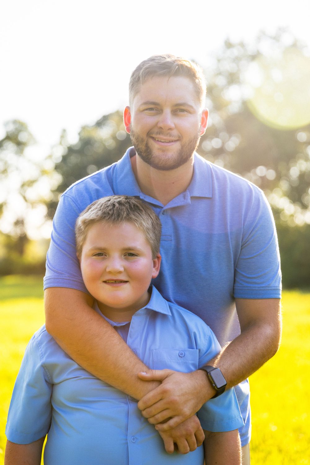 A tender portrait of parent and child in matching blue polo shirts standing in golden sunlight.