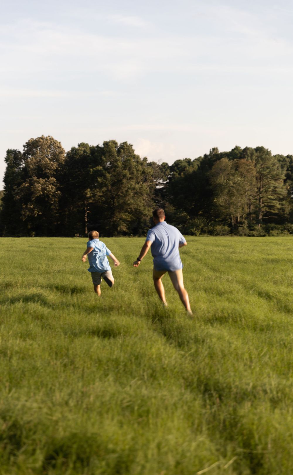 Two people running playfully through a lush green field on a sunny day.