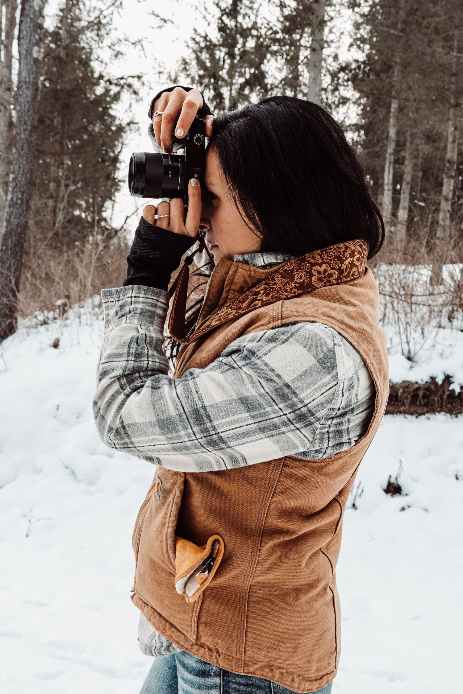 Photographer taking pictures in snowy winter forest wearing plaid and brown vest.