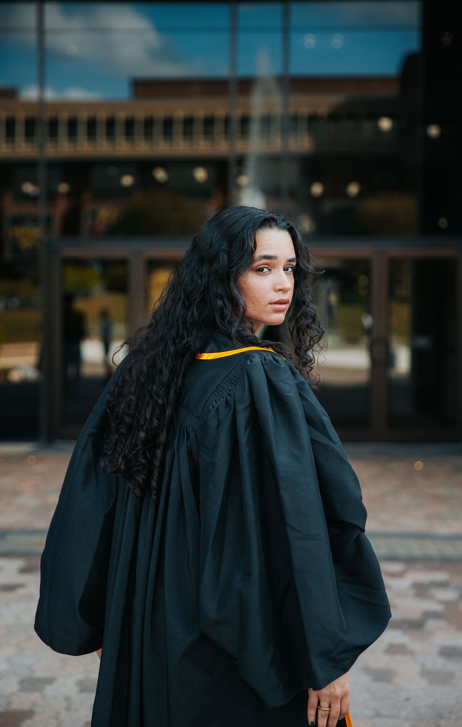 Artistic graduation portraits featuring flowing black robes and gold accents against modern architecture.