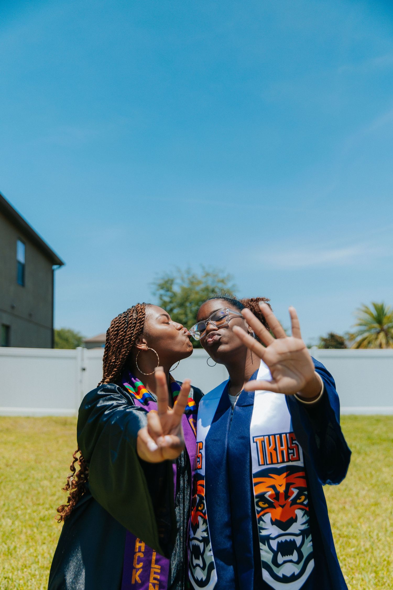 Two graduates in academic regalia posing playfully outdoors.