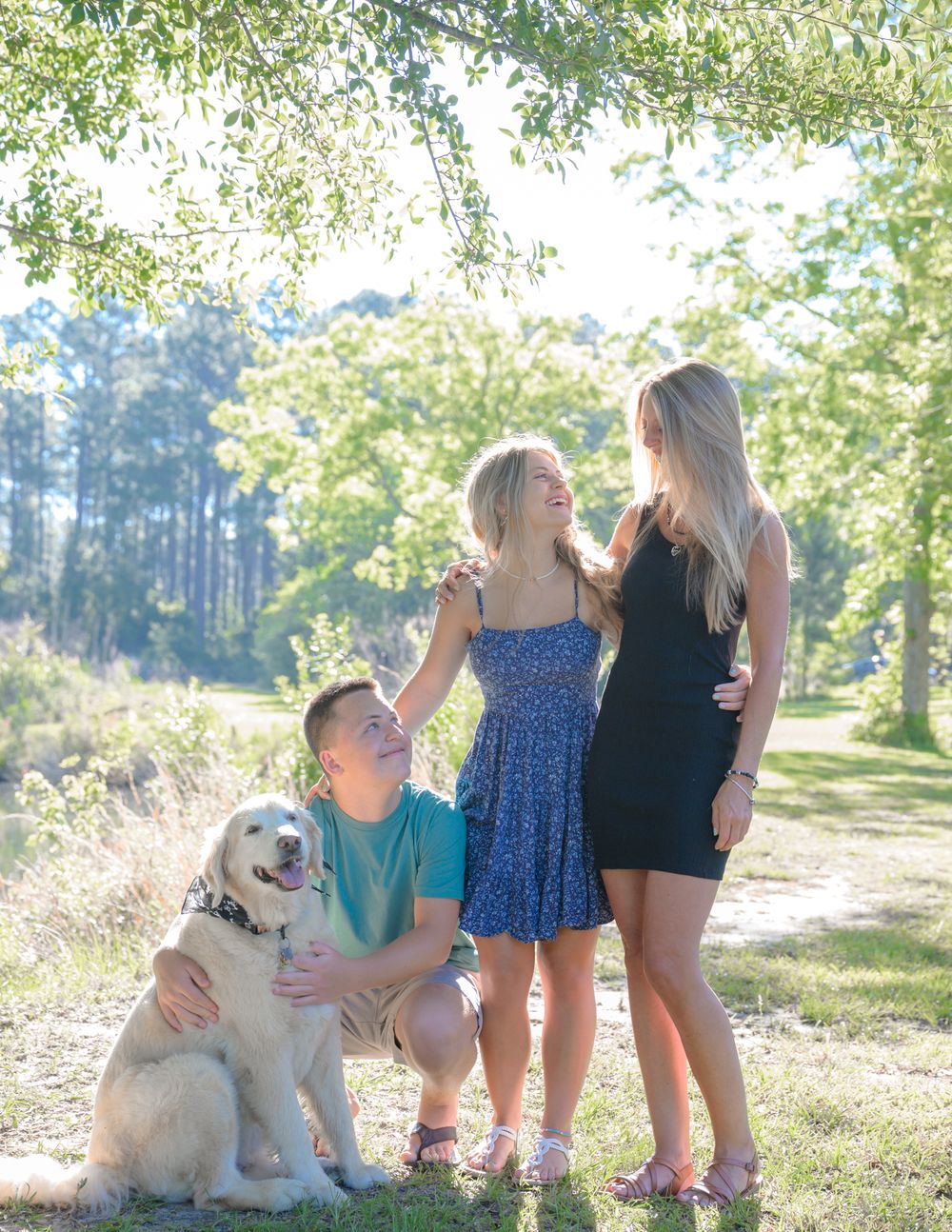 A group poses with their golden retriever in a sunlit park setting.