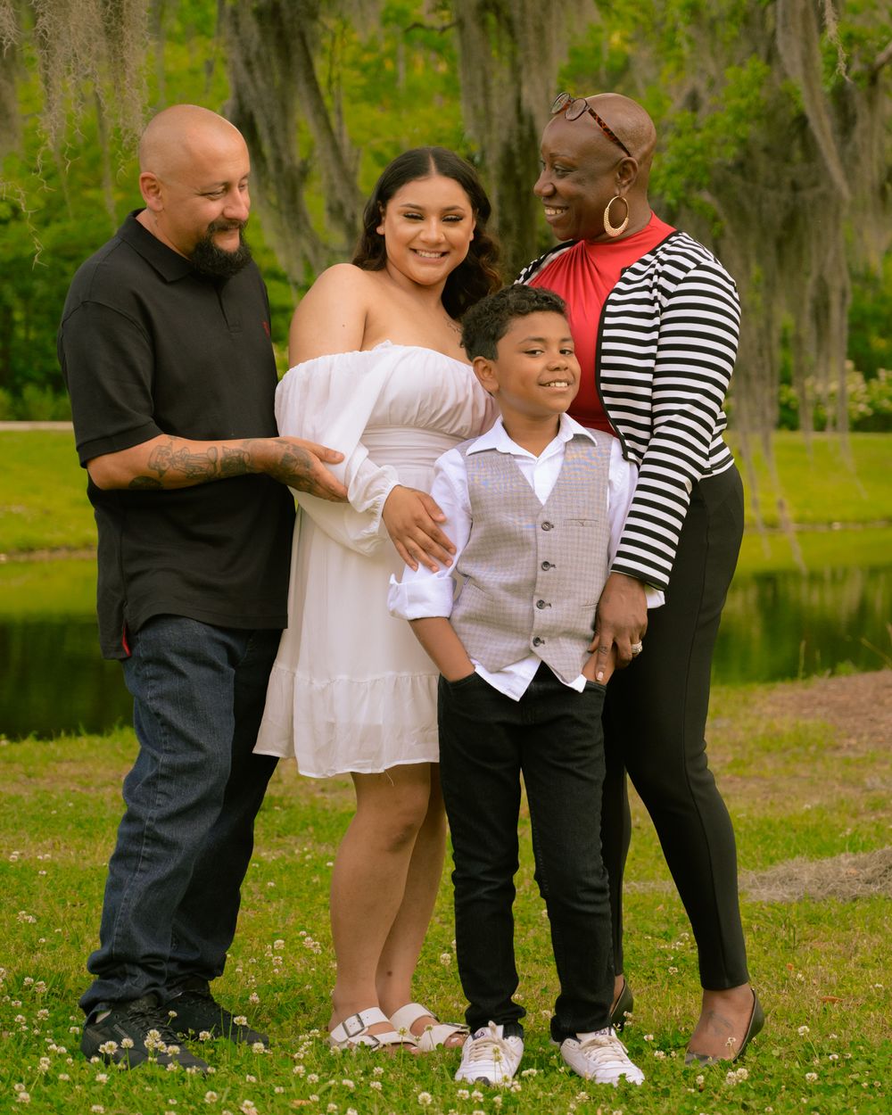 A small group poses together on grass with Spanish moss-draped trees and a pond in the background.