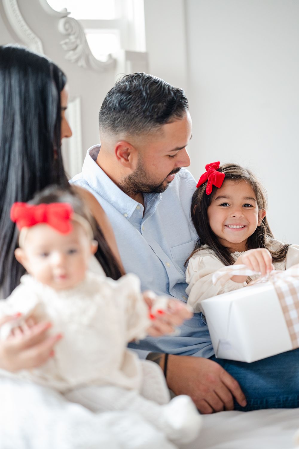A family sits together on a white couch, sharing a joyful moment while wearing matching white and red outfits.