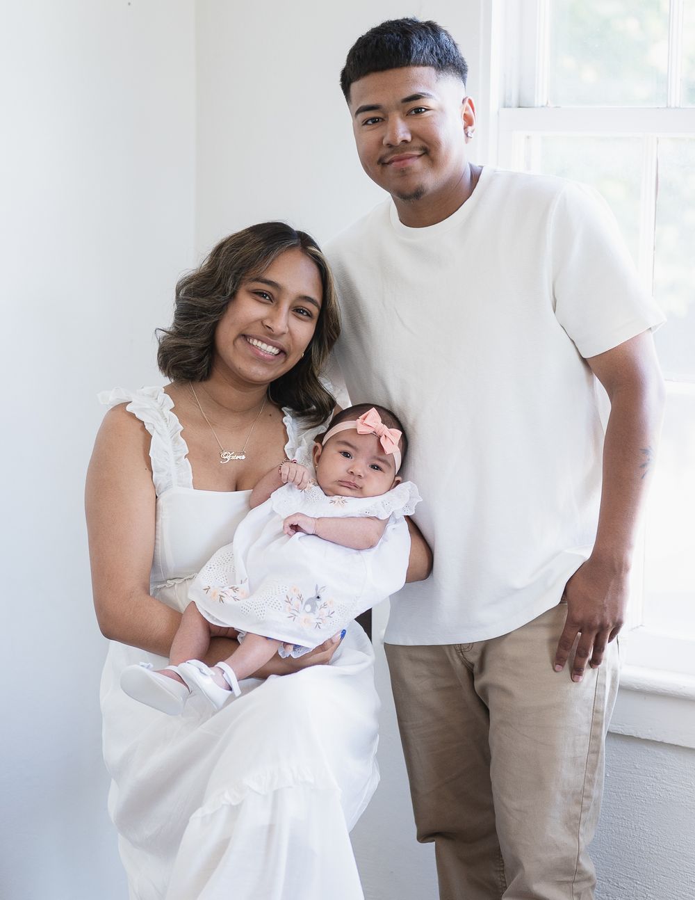 Family poses together in white room for baby portraits.