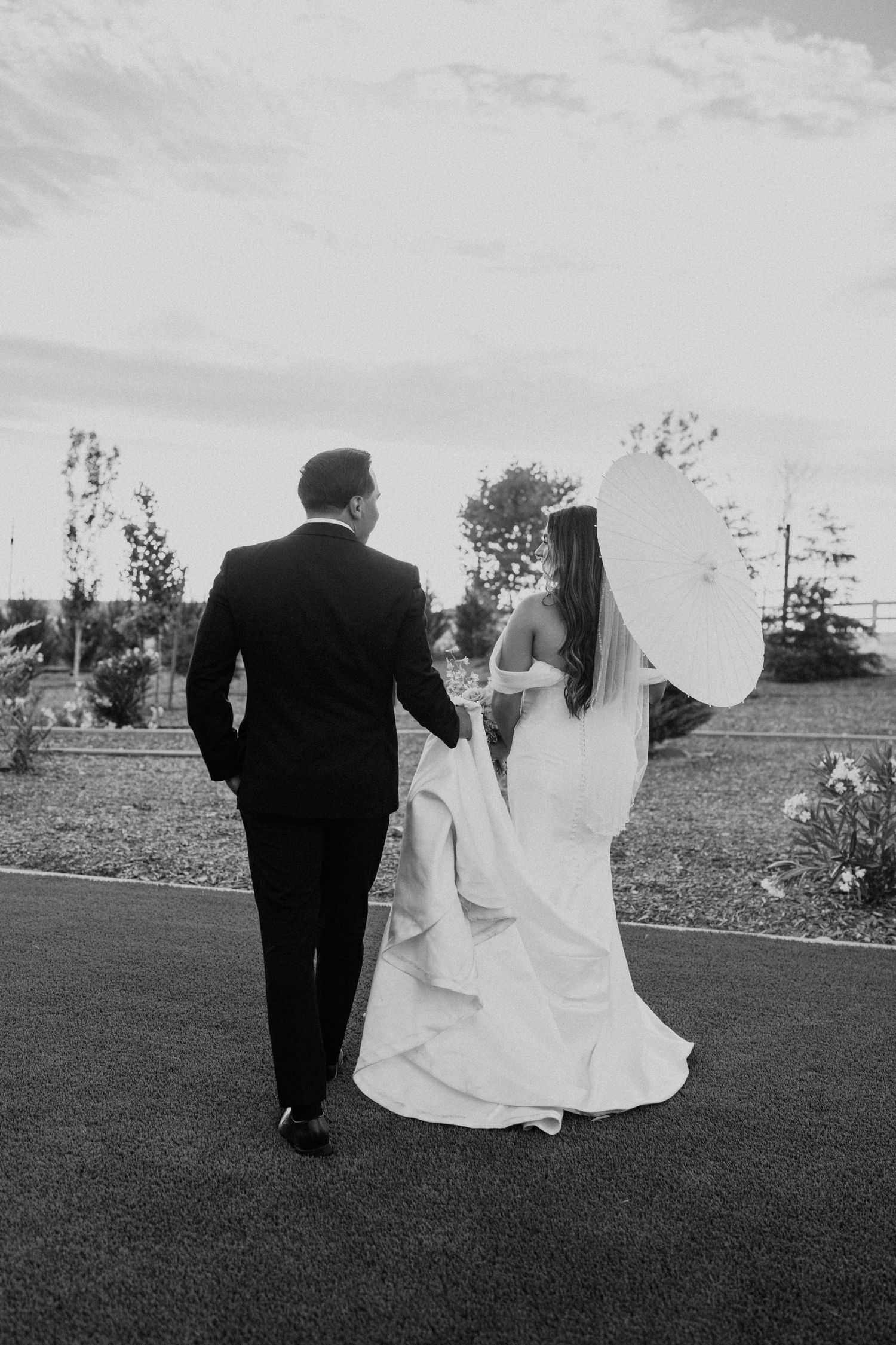 A romantic black and white photo of newlyweds holding hands while walking together, the bride in a flowing veil.