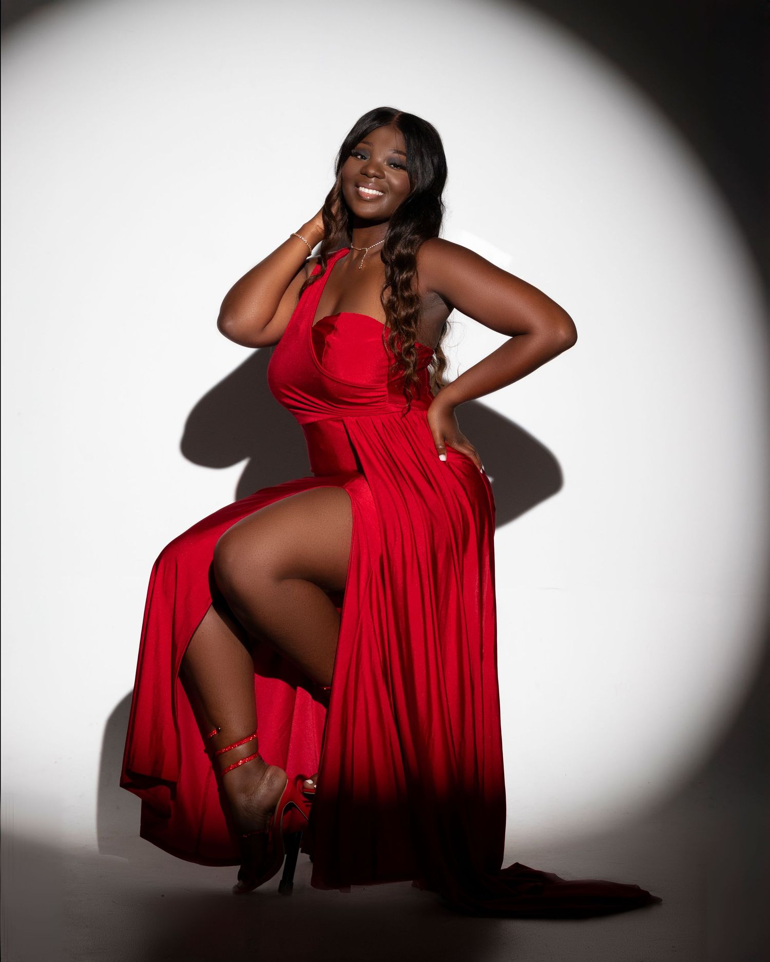 Glamour portrait of someone in flowing red gown against white backdrop with dramatic lighting.