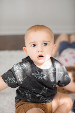 A baby wearing a black shirt with white dinosaur prints crawls on a light colored surface.
