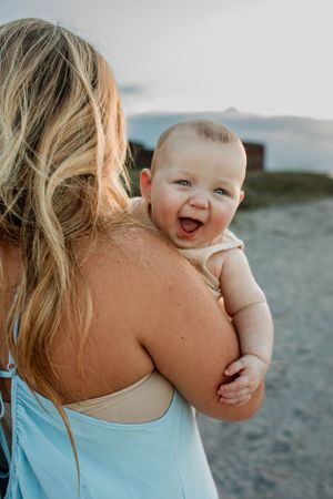 Joy-filled baby laughing while being held at the beach during sunset.