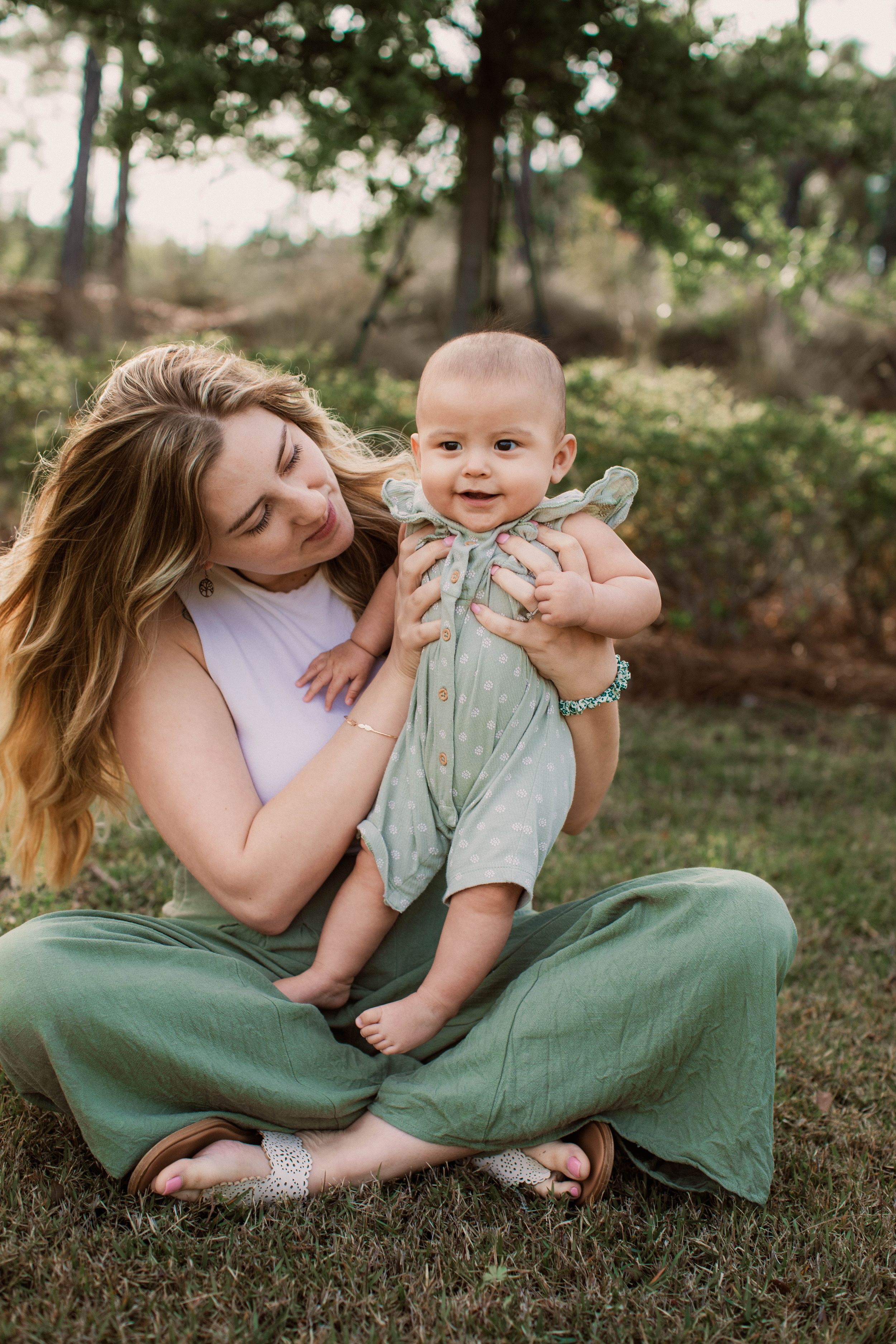 Parent and baby sharing joyful moment while sitting on grass in outdoor setting.