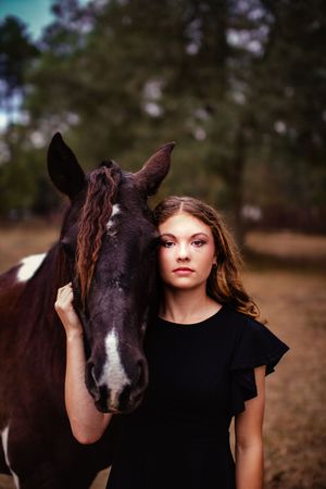 A brown and white horse stands close beside someone wearing a black shirt in an outdoor portrait setting.