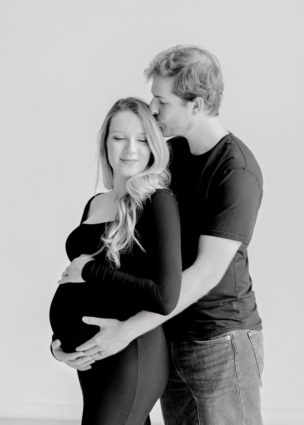 Black and white maternity photo showing a couple embracing with hands on pregnant belly.