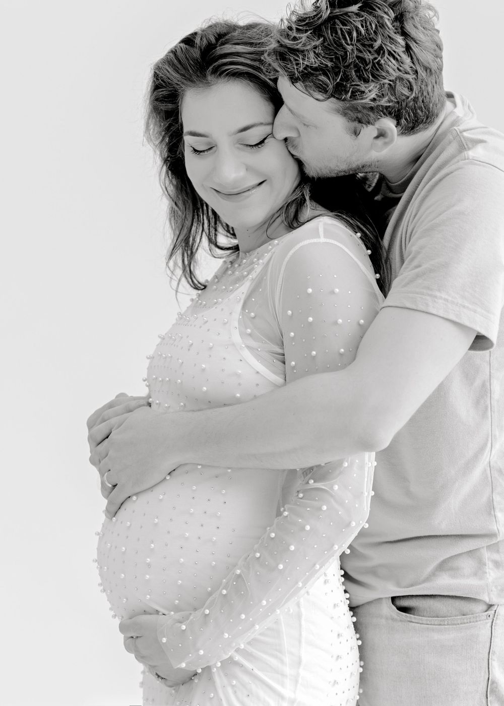Black and white maternity photo showing couple embracing with baby bump.
