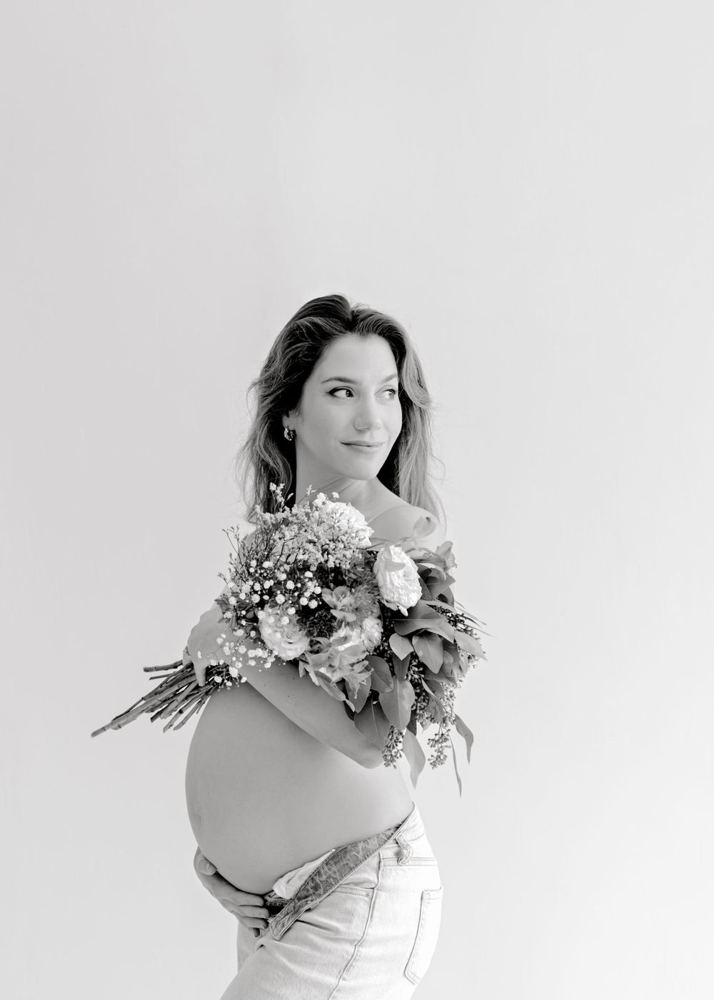Black and white maternity portrait with woman holding floral bouquet.
