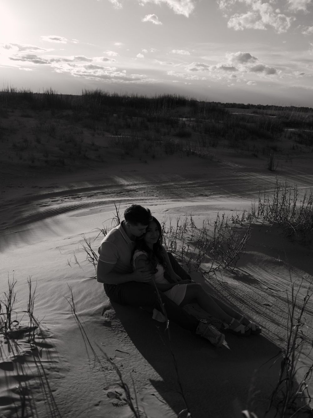 Silhouette of a person sitting by a lake during sunset at dusk in a moody black and white scene.