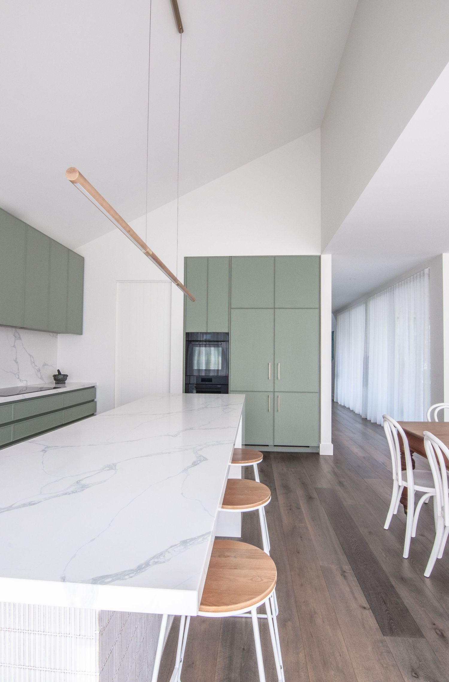 Sleek kitchen featuring sage green cabinets, white marble countertops, and wooden bar stools.