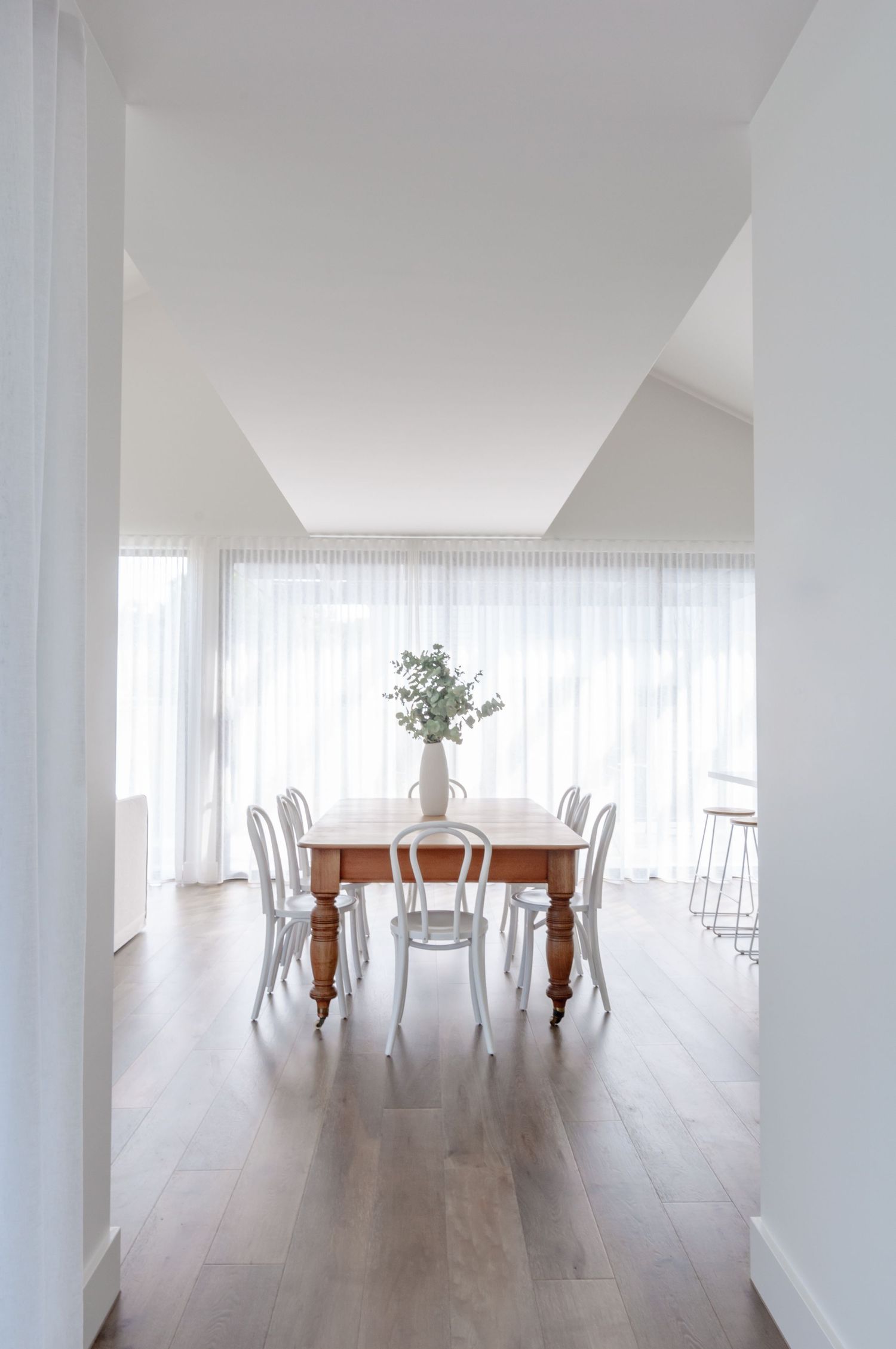 Bright dining area with wooden table, white chairs, and sheer curtains filtering natural light.