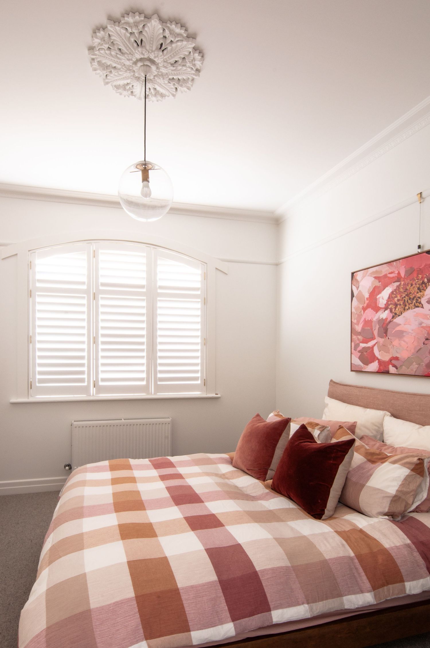 Cozy bedroom with ornate ceiling medallion, white shutters, and pink plaid bedding.