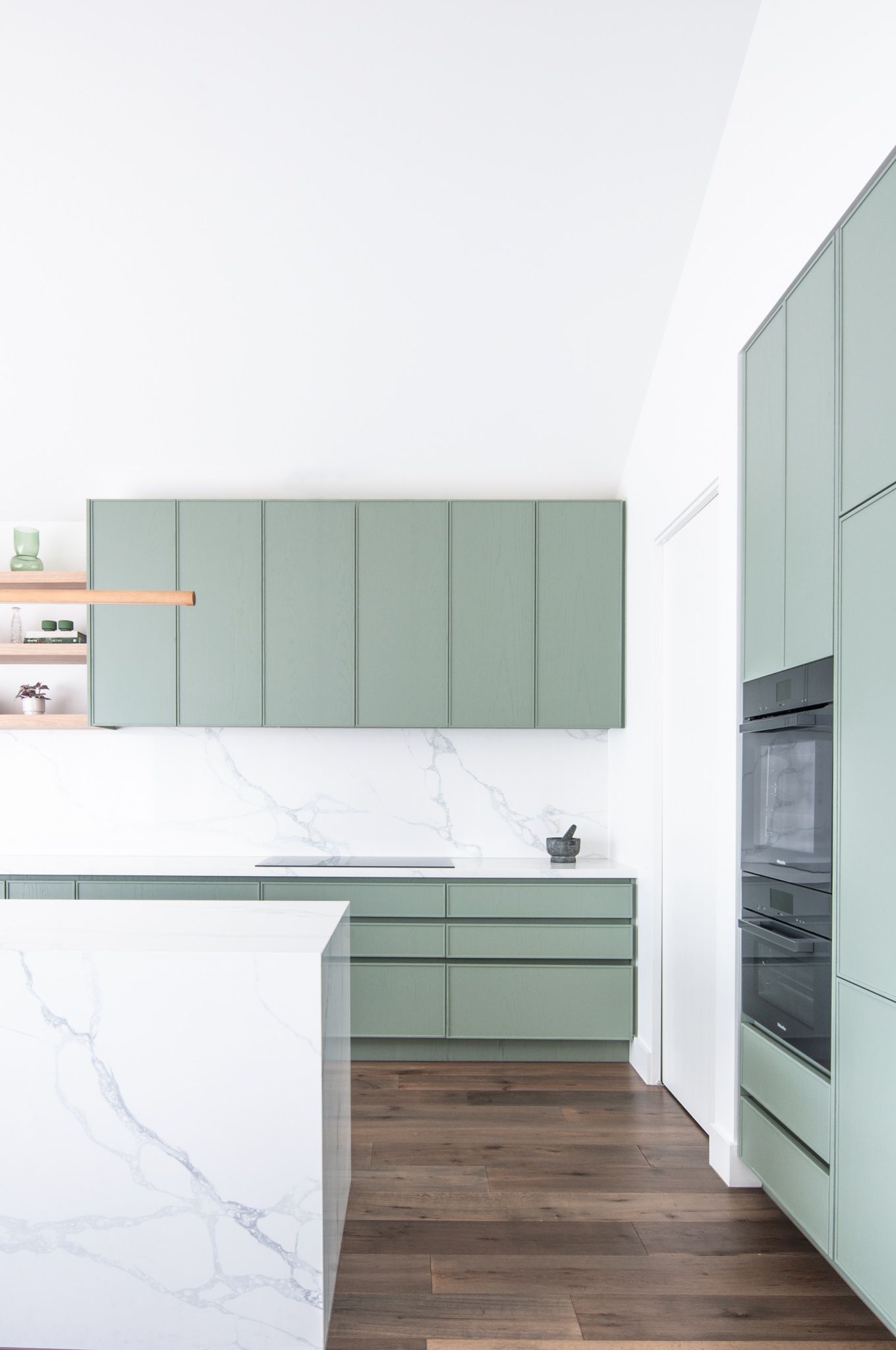 Minimalist kitchen design with sage green cabinets, marble countertops, and hardwood flooring.