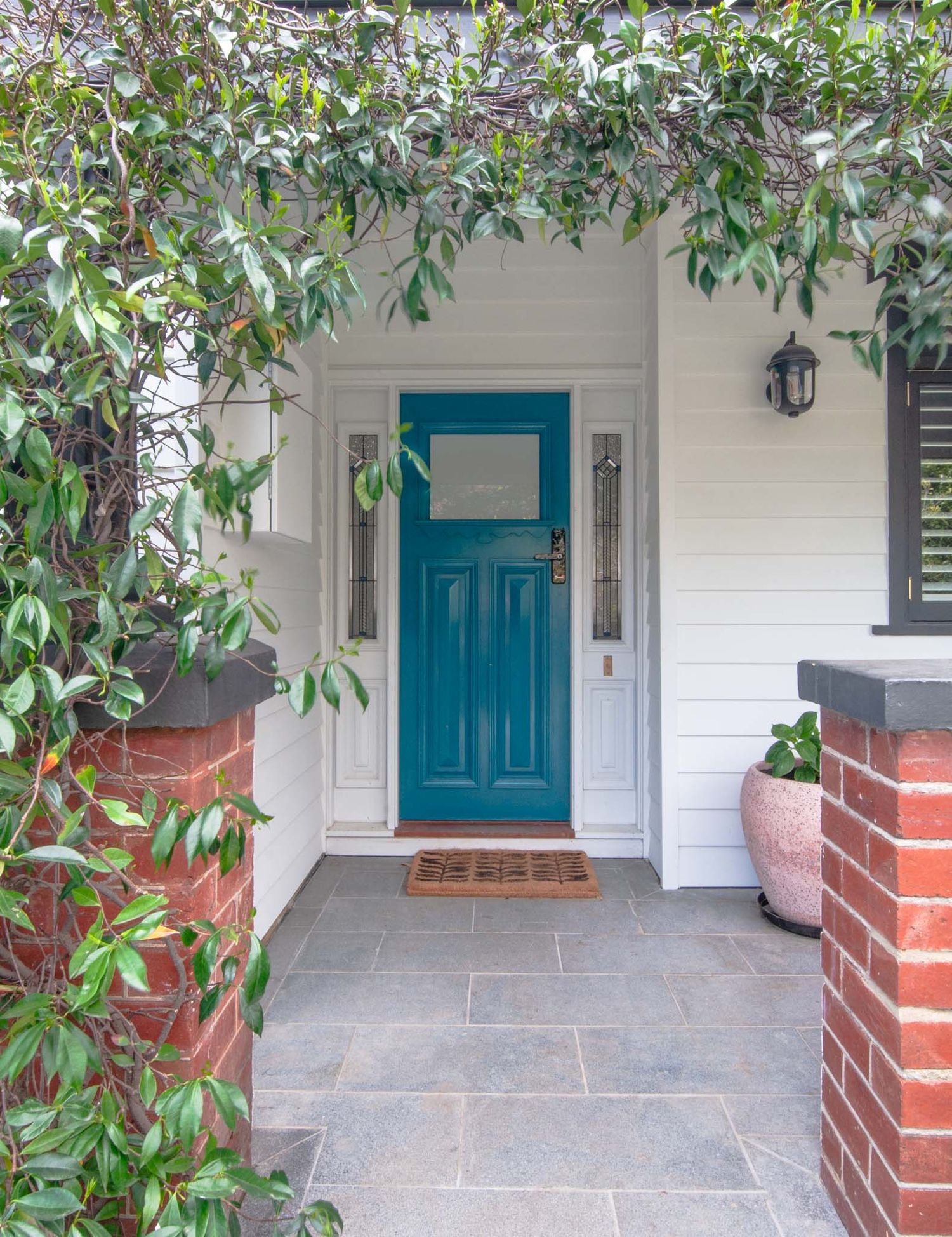 Charming house entrance with turquoise door framed by lush climbing vines and brick pillars.
