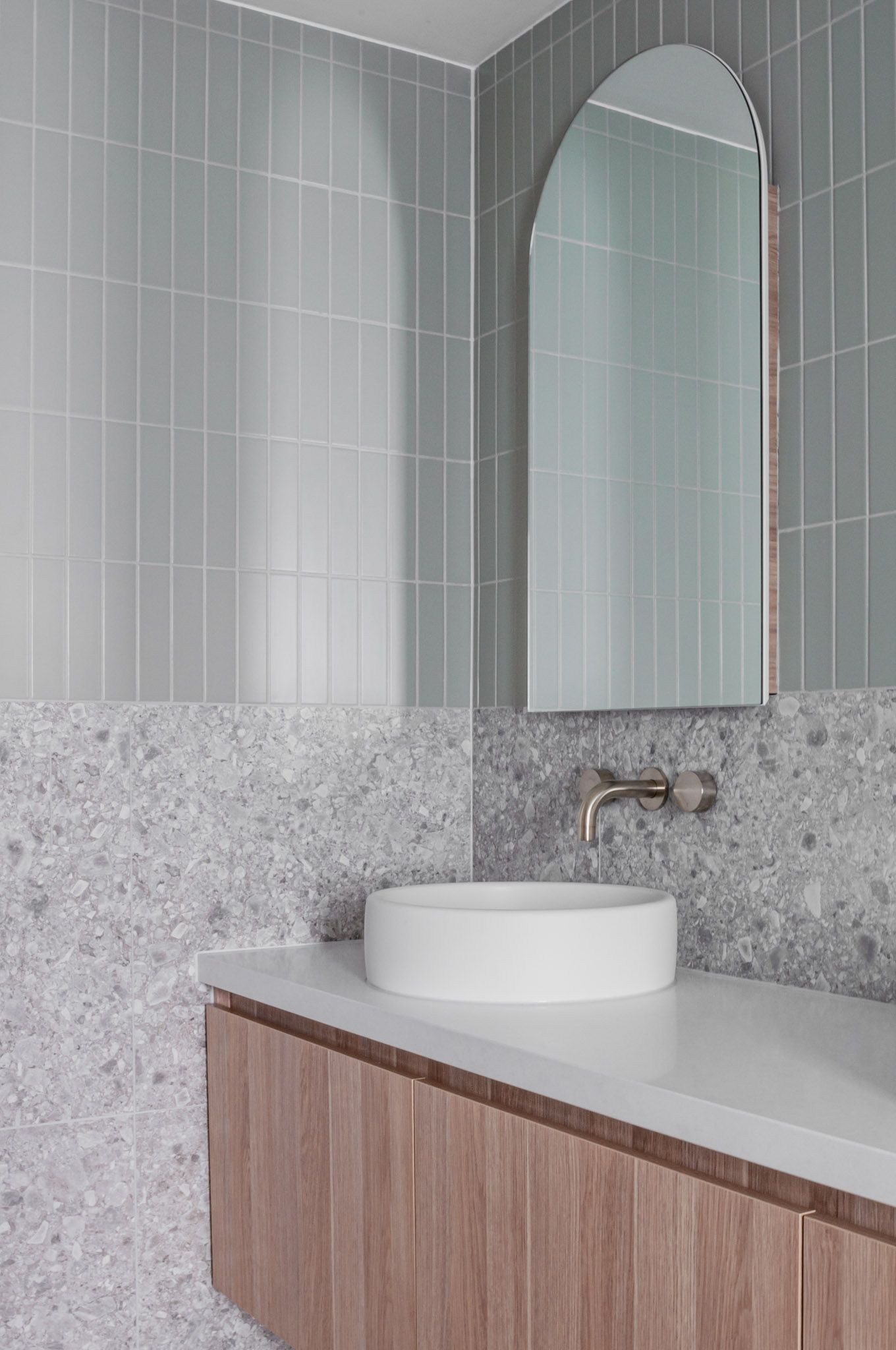 Contemporary bathroom featuring grey tiles, terrazzo details, and floating wooden vanity with vessel sink.