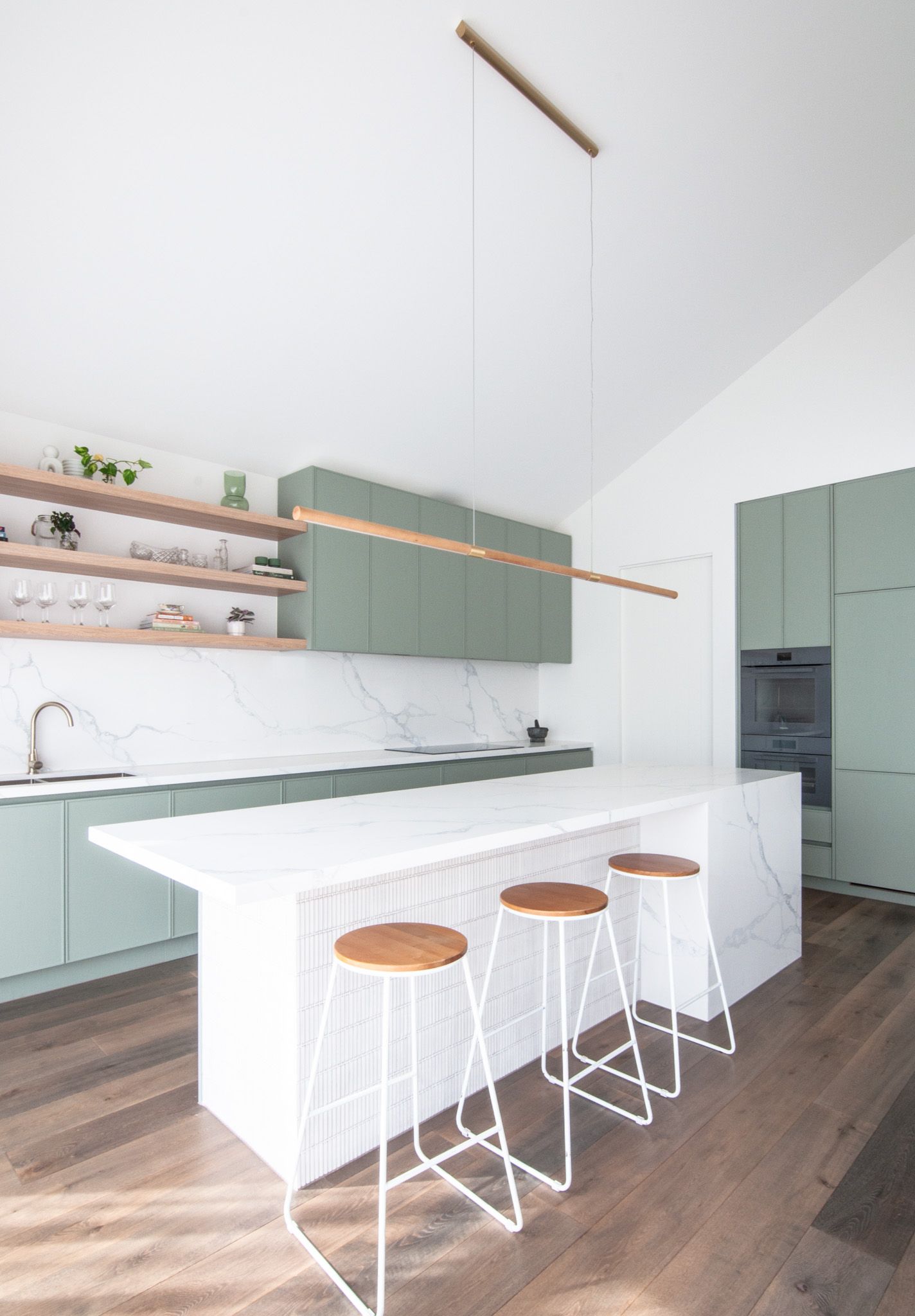 Sleek kitchen island with white bar stools and sage green cabinetry in an open-concept space.