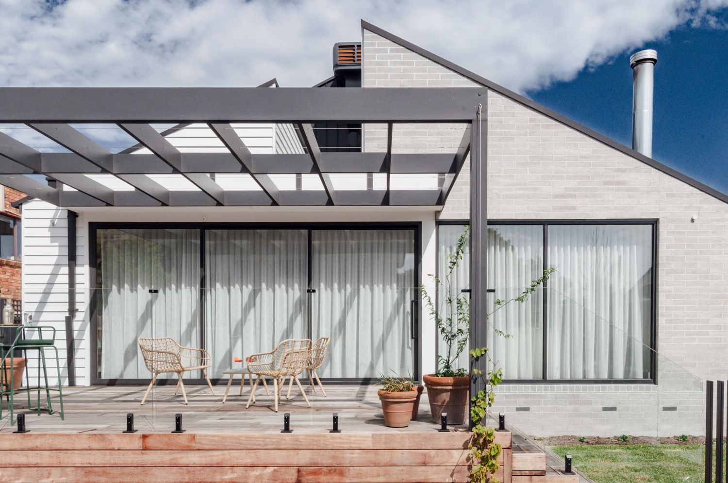 Contemporary home exterior with pergola, white walls, and floor-to-ceiling windows facing a wooden deck.