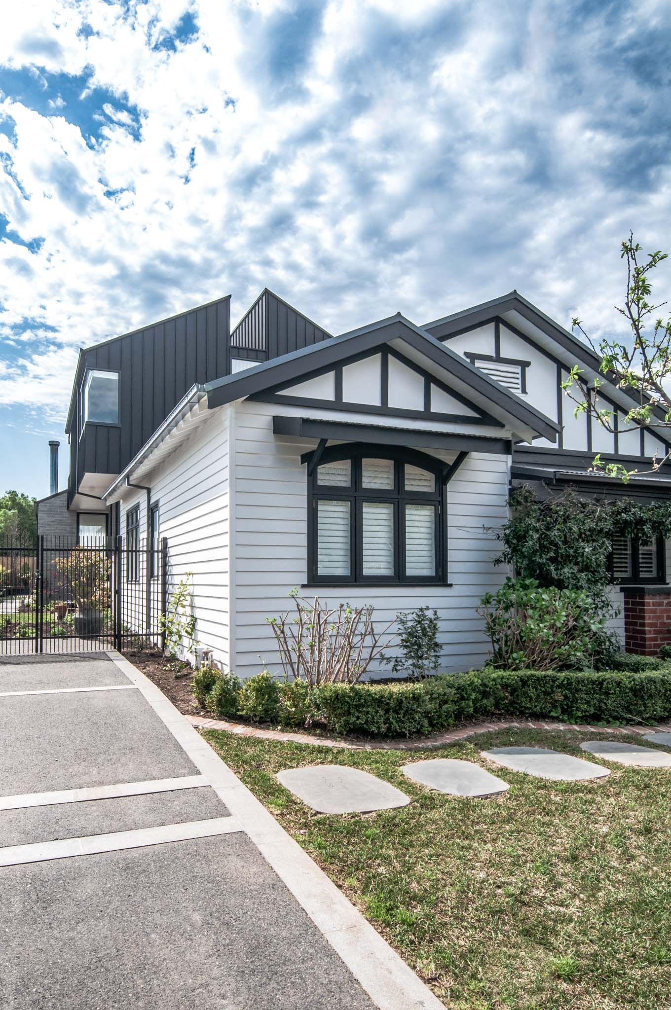 Modern white house with black accents featuring architectural details and stone pathway in the front yard.