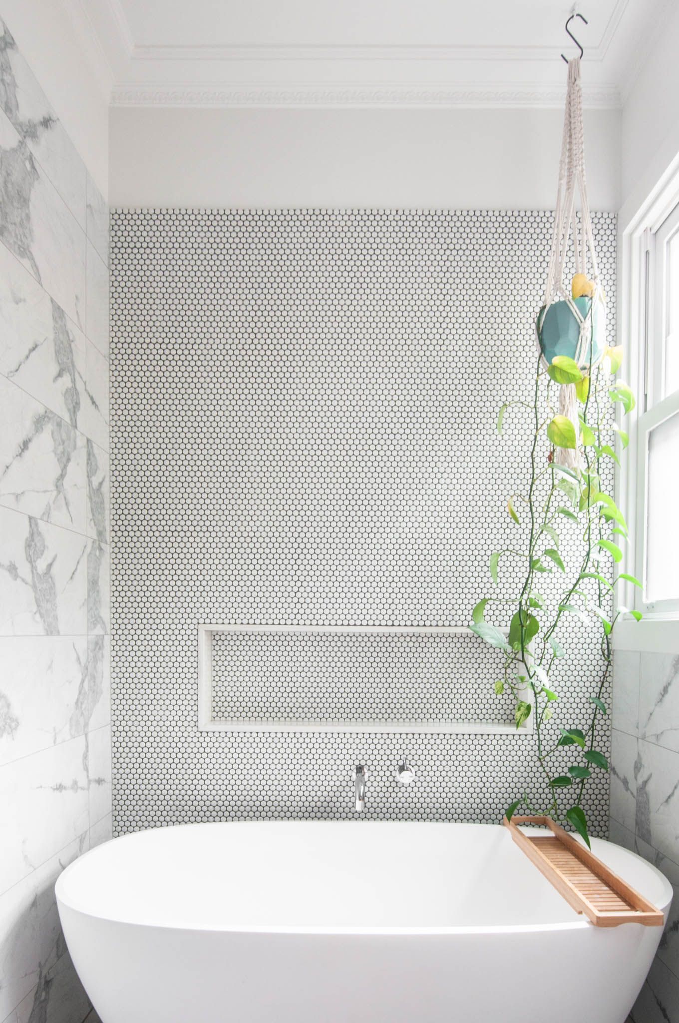 Freestanding white bathtub against marble and penny tile walls with climbing vine decor.
