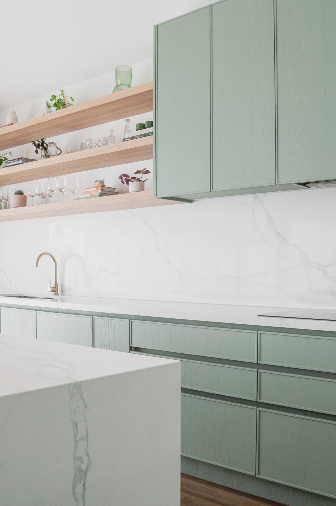 Modern kitchen featuring sage green cabinets, marble countertops, and wooden open shelving.