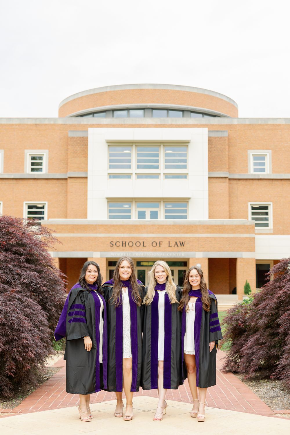 Law school graduates in purple and black robes pose together outside their school building.