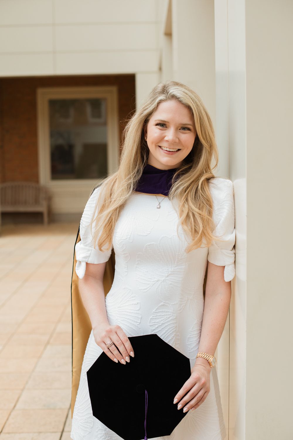 A graduate in white attire poses confidently against a classical architectural backdrop.