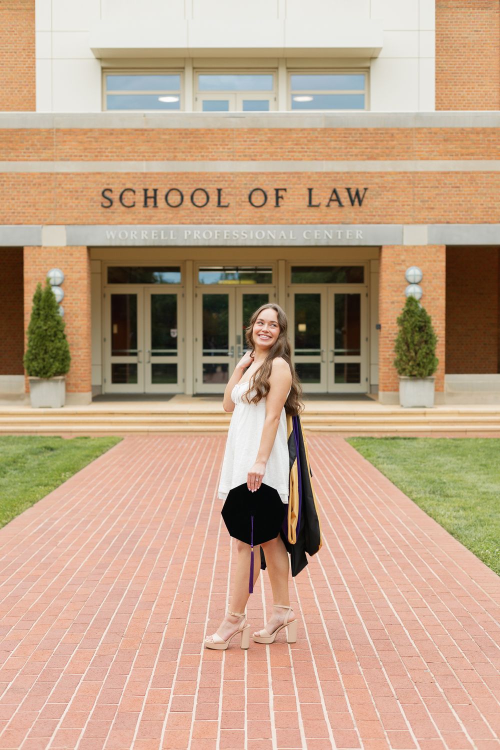 A graduate celebrates their achievement outside the School of Law building.