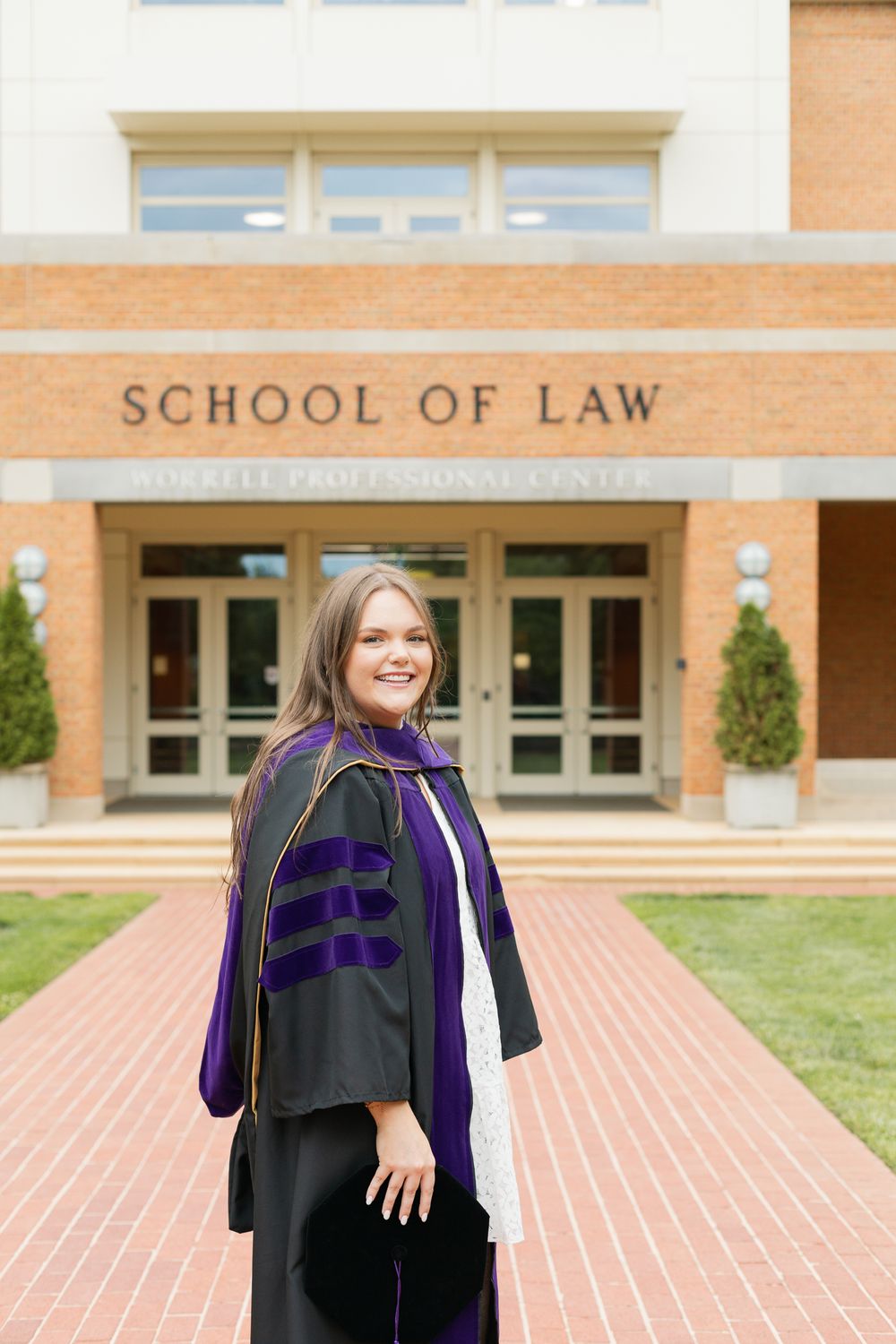Graduate in academic regalia stands proudly in front of School of Law building entrance.