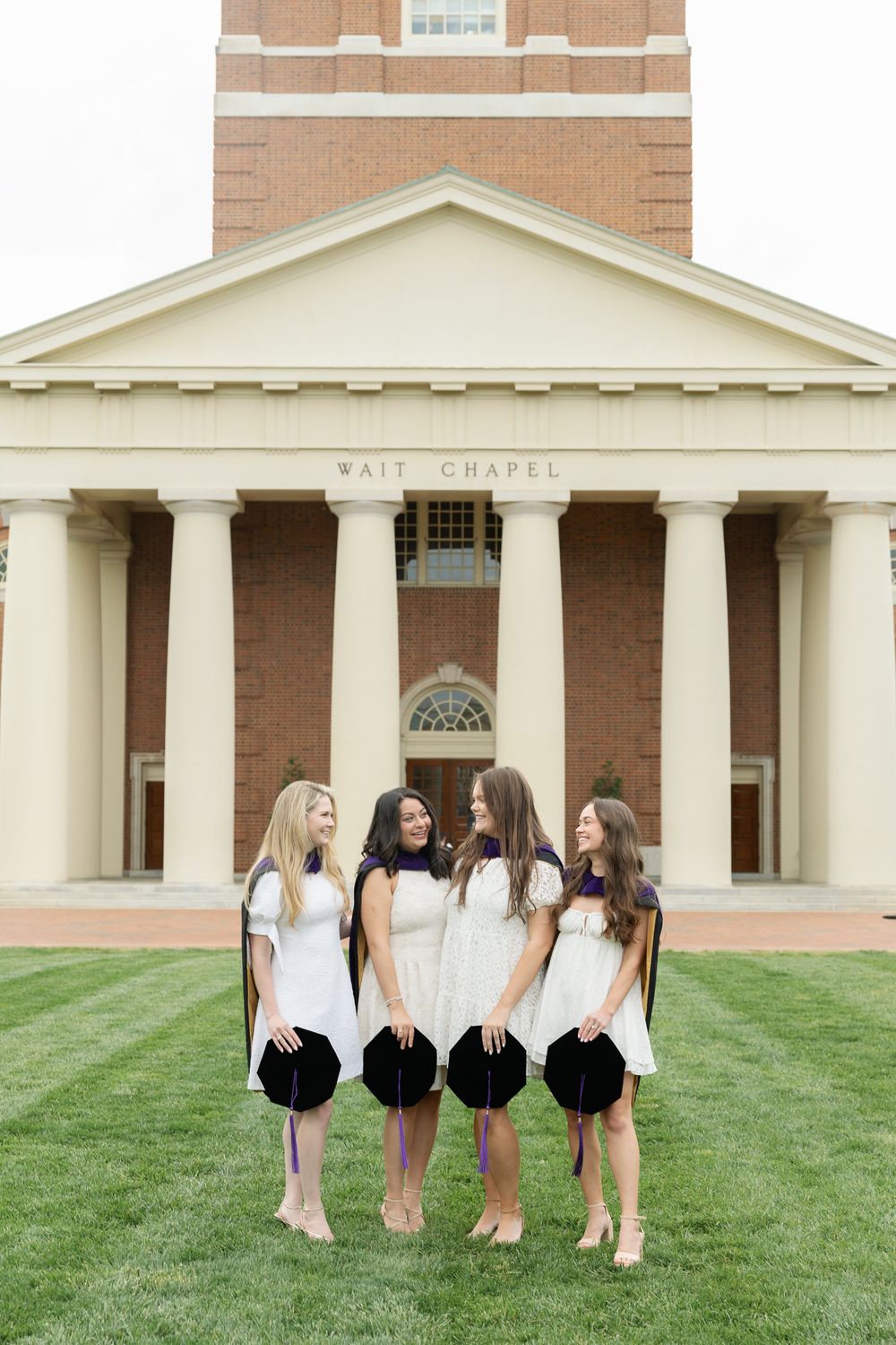 Group of graduates in white dresses pose together in front of Wait Chapel's classical columns.