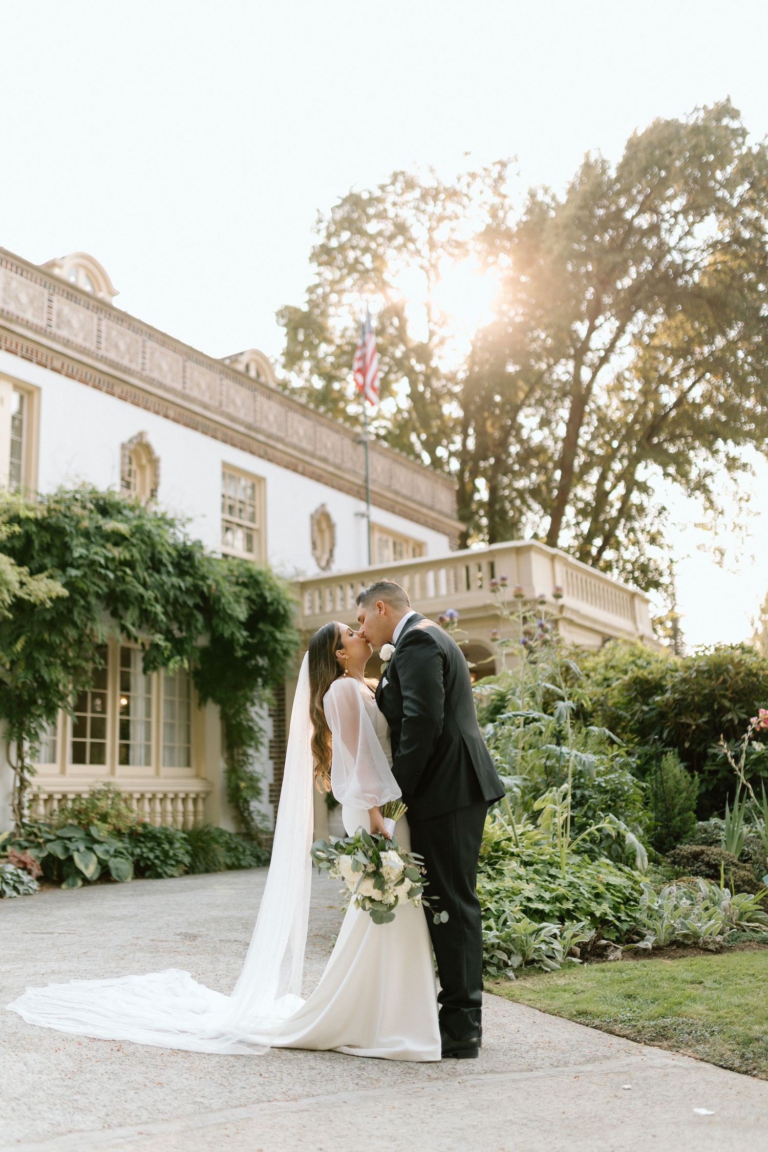 A classic wedding portrait in front of an elegant white mansion with lush gardens.