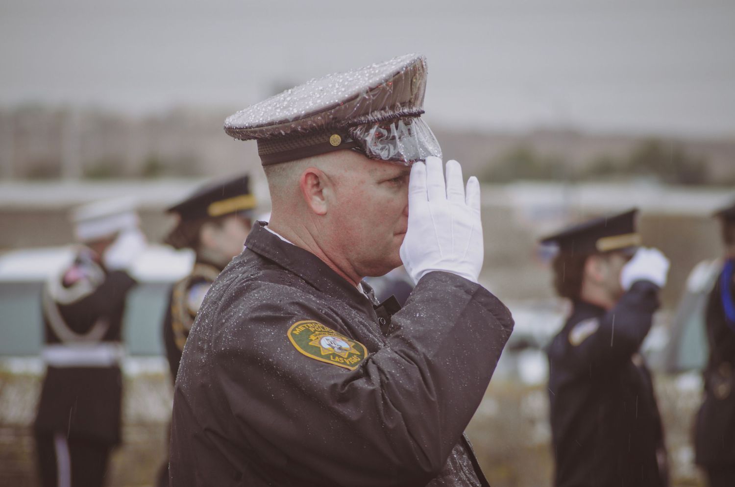 Line of uniformed officers saluting during outdoor ceremony.