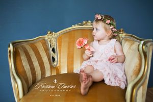 Baby wearing floral crown sits on vintage gold striped sofa.